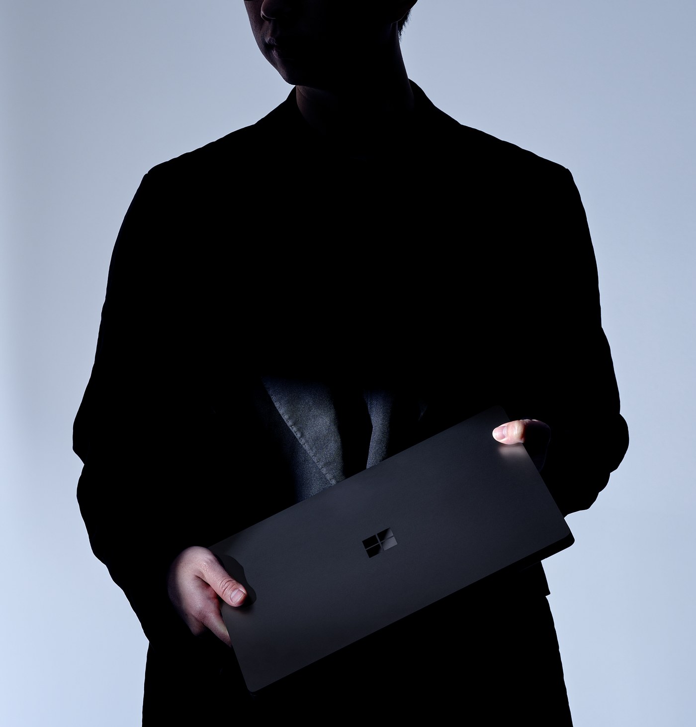 A closed Nightfall Surface Laptop Ultra held at the side